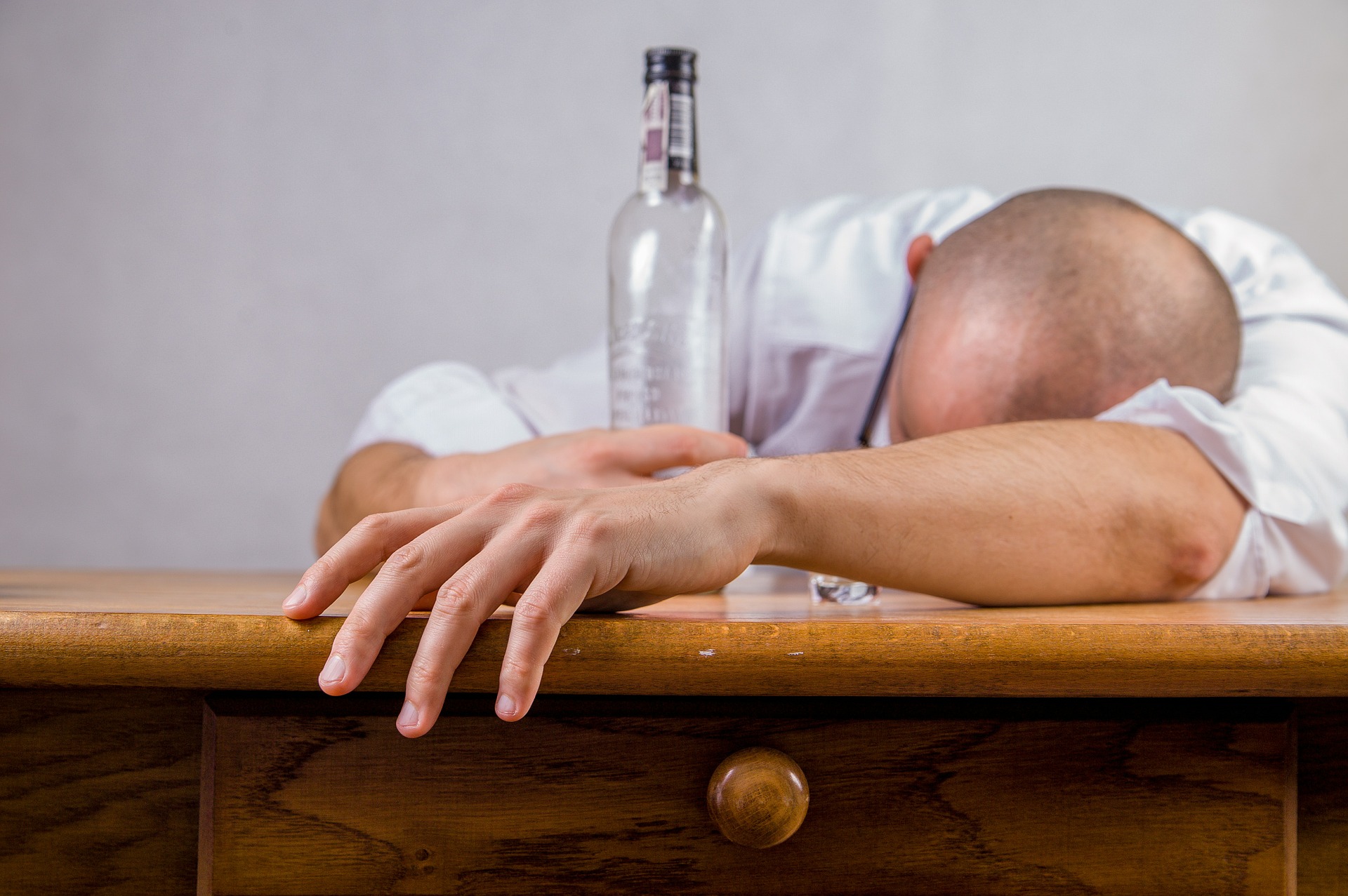 A man slumped over a bar, one hand holding an empty bottle.
